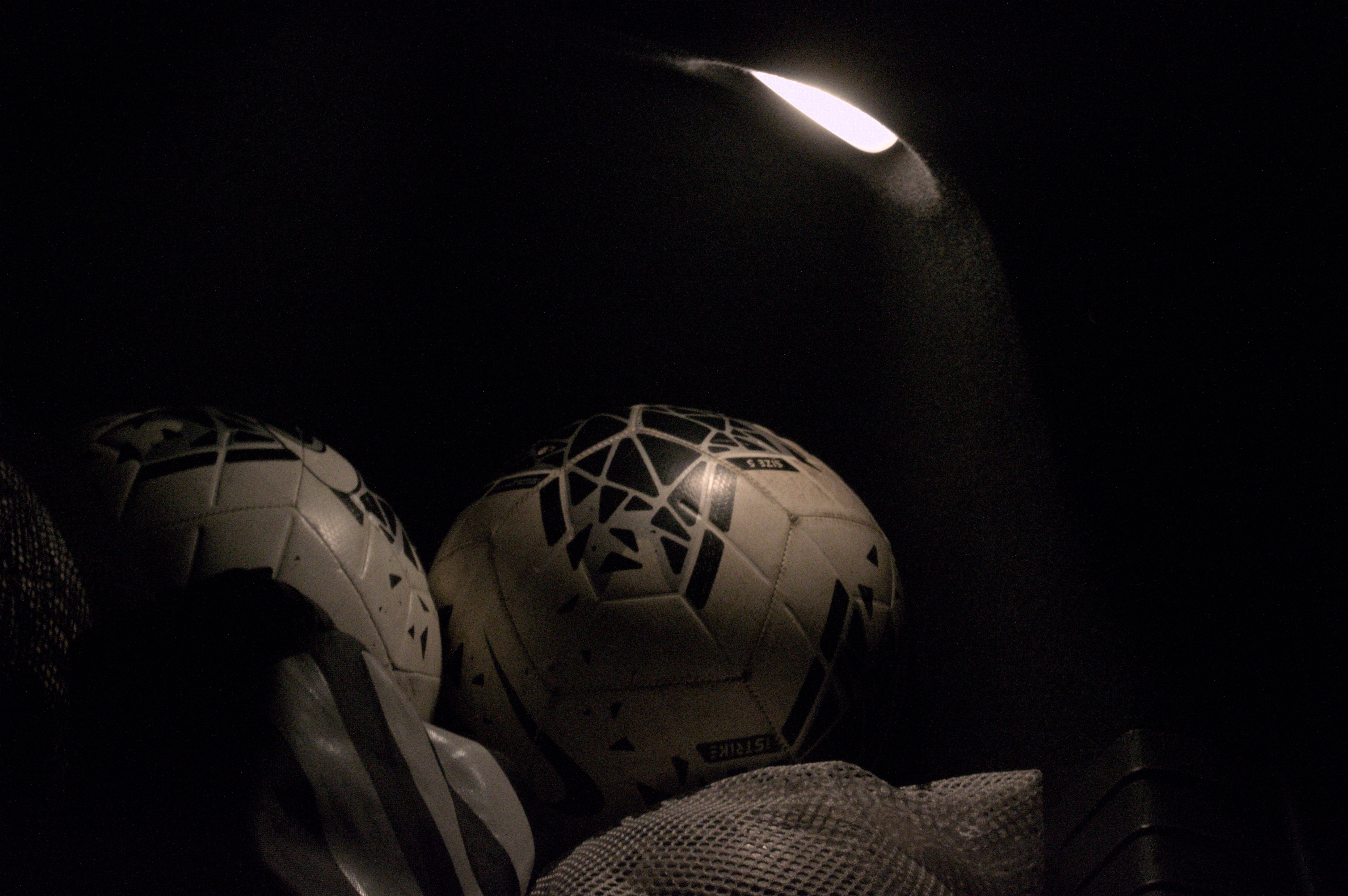 Photo of several soccerballs in a trunk of a car with a single warm light illuminating them